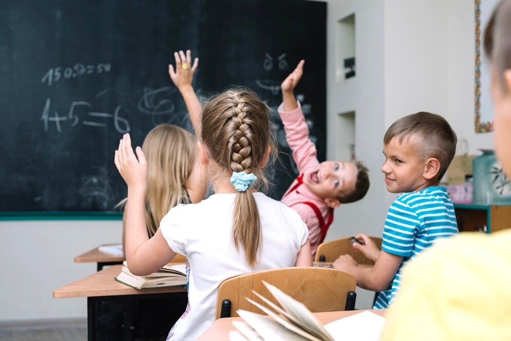 alunos-sentados-em-sala-de-aula-levantando-as-maos_23-2147663514