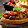 Bruschetta caponata with raisins and pine nuts decorated with a leaf of basil