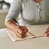 African american woman writing on notebook sitting on table at home