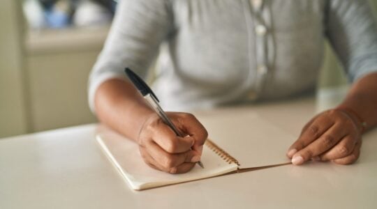 African american woman writing on notebook sitting on table at home