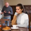 Woman sitting at table, unhappy family quarrelling on backgroud