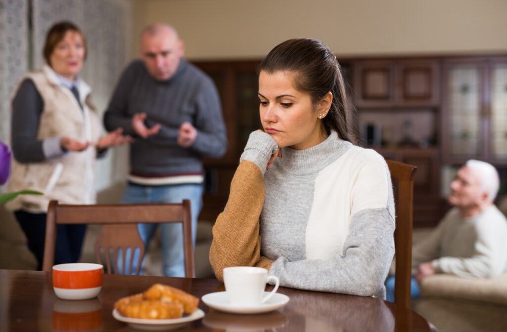 Woman sitting at table, unhappy family quarrelling on backgroud