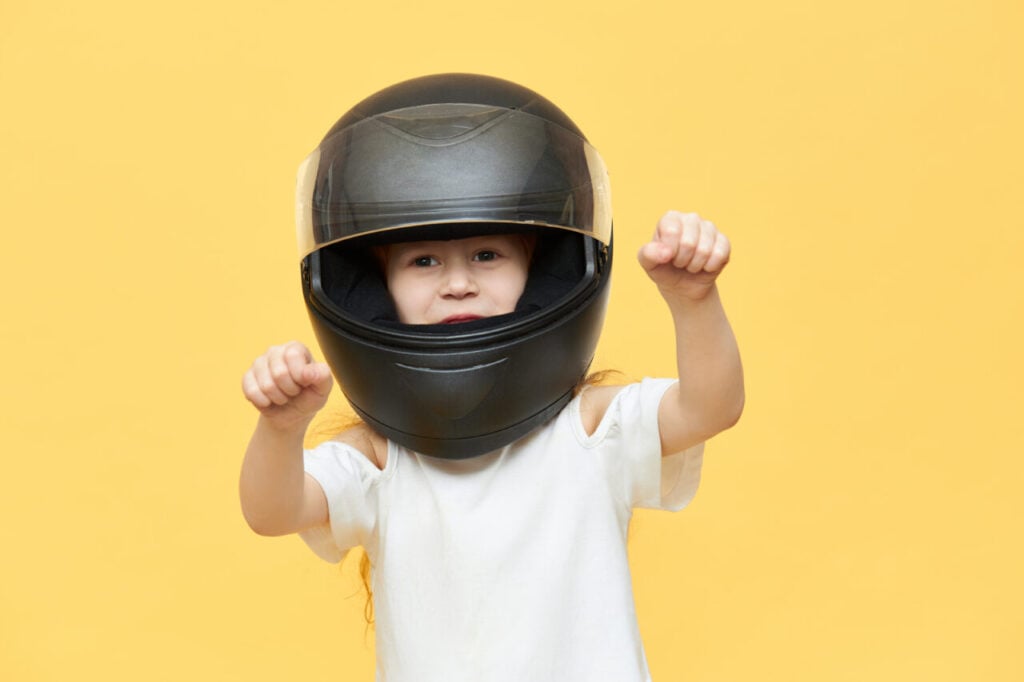 Skillful experienced little girl in safety motorcycle helmet driving motor vehicle very fast, holding hands on steering wheel on handlebar, enjoying high speed. Extreme sports and active lifestyle