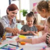 Group of small nursery school children with teacher indoors in classroom, painting.